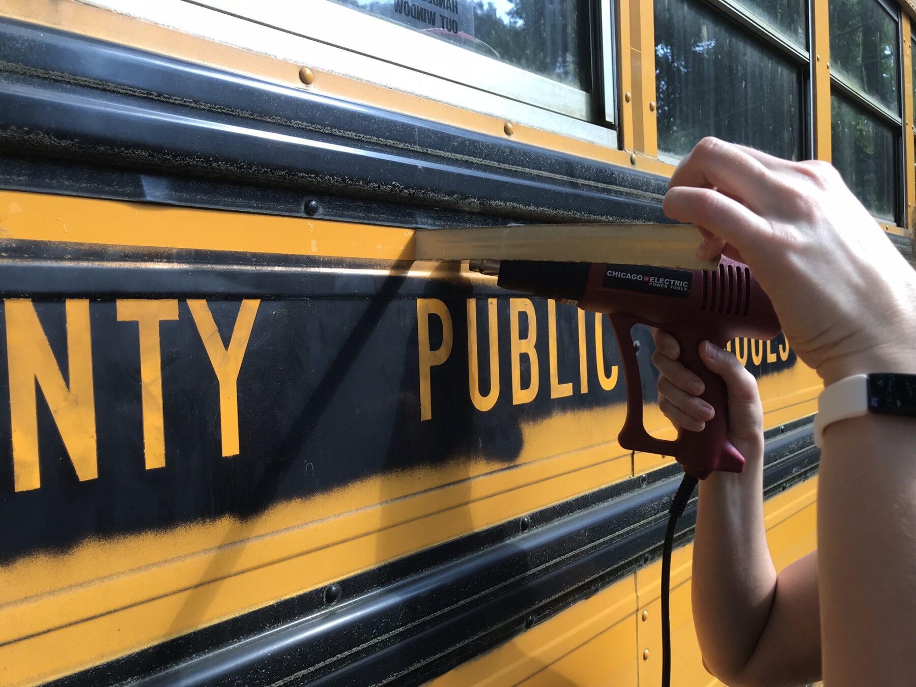 Using a heat gun to remove reflective tape from the bus
